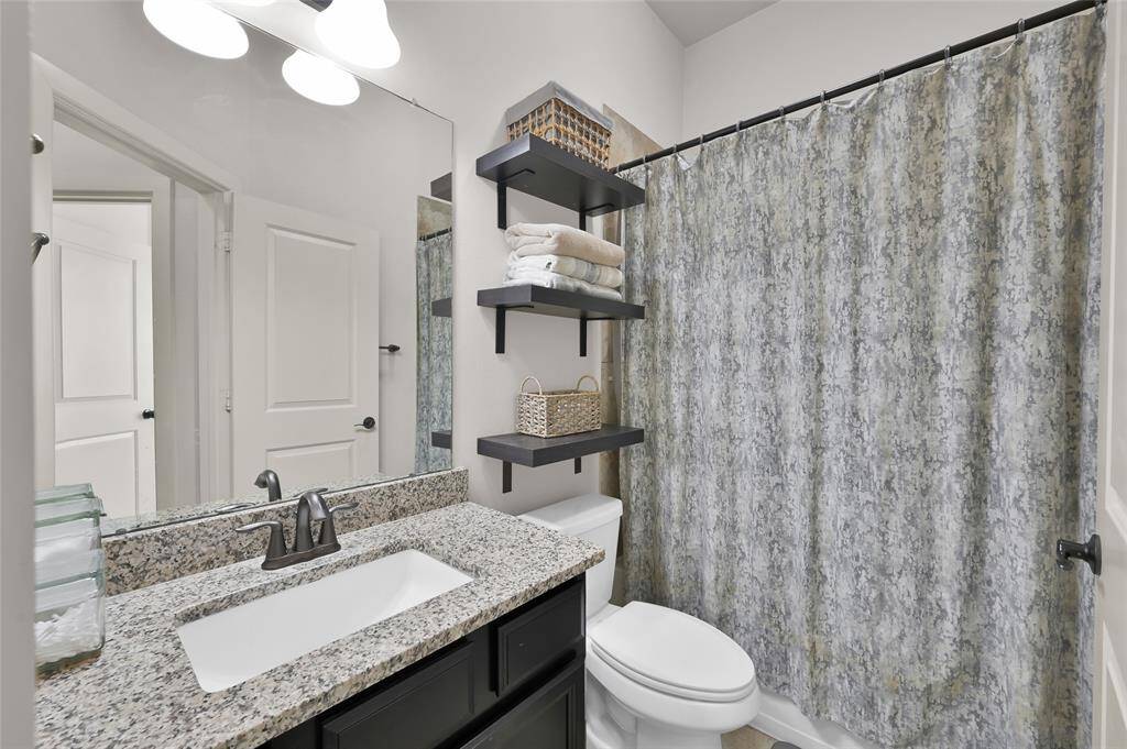 This secondary bathroom features a modern design with a granite countertop, a sleek undermount sink, and a stylish faucet and a shower/tub combo.