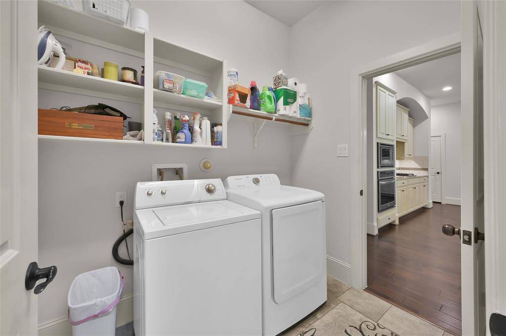 Spacious laundry room with plenty of room for the washer and dryer, open shelving for storage and cabinetry with two access points from the kitchen and the primary bedroom.