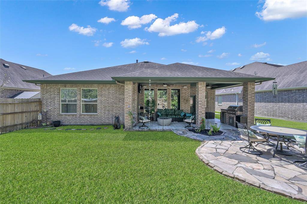 This backyard offers a spacious, well-maintained lawn with a cozy covered patio featuring outdoor seating. The area includes a built-in grill station and a charming stone patio with a dining set, perfect for entertaining. The space is bordered by a wooden fence, ensuring privacy.