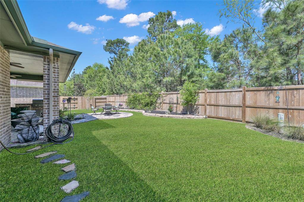 This backyard features a spacious, well-maintained lawn with a stone path leading to a cozy seating area. It's enclosed by a wooden fence and surrounded by mature trees, offering privacy and a peaceful atmosphere.