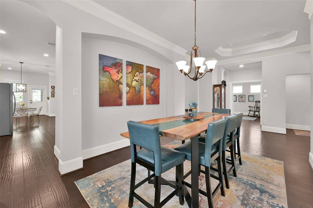 Formal dining area with plenty of room for a large table and accented by a modern light fixture. The space is enhanced by light walls and dark wood flooring. The open layout leads to the kitchen, creating a welcoming and cohesive living space.