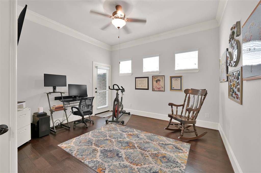 Bright home office space with hardwood floors, a ceiling fan, and ample natural light from three high-set windows. A door leads to a small outside space for relaxing and fresh air.