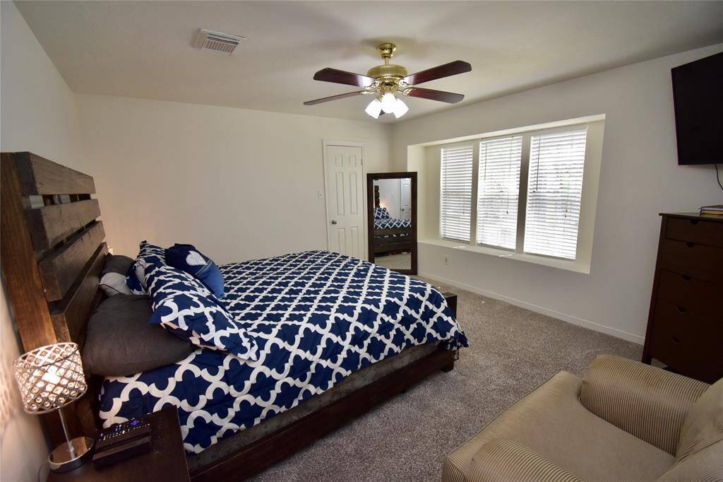 This primary bedroom upstairs features abundant space and a ceiling fan. It has three large windows providing natural light, and plush carpet.