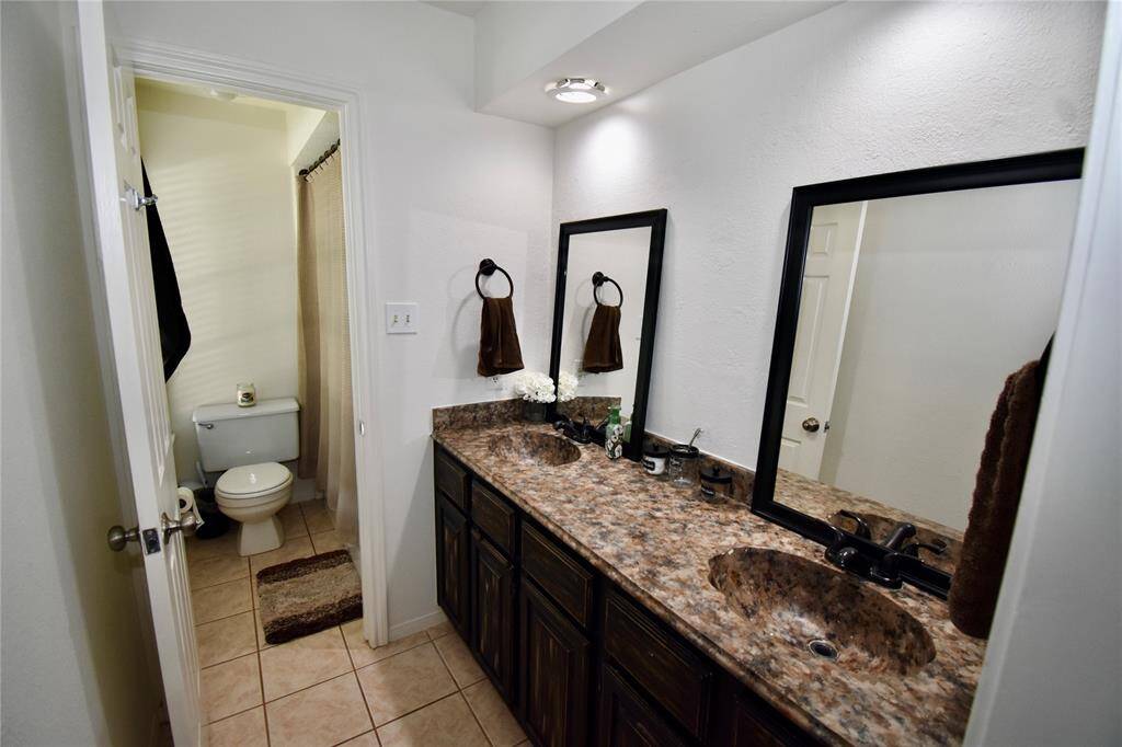 This spacious bathroom features a shower / tub combo, and dual topped vanities with ample storage, all enhanced by natural light from a sizable window.