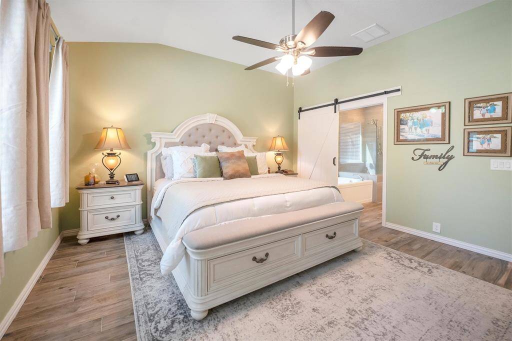 This luxurious suite features wood-look tile flooring, neutral paint, and a wall of windows that frame peaceful views of the backyard. A modern sliding barn door leads to the spa-like ensuite, creating the perfect blend of comfort and style.