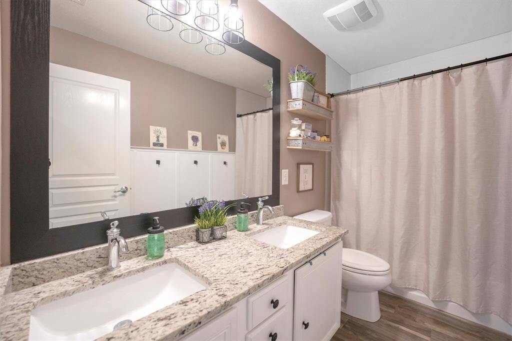 The full bathroom upstairs is easy to share, featuring a dual-sink vanity with ample storage, a framed mirror, and designer vanity lighting above. A convenient tub/shower enclosure adds function and flexibility for busy mornings or relaxing evenings.
