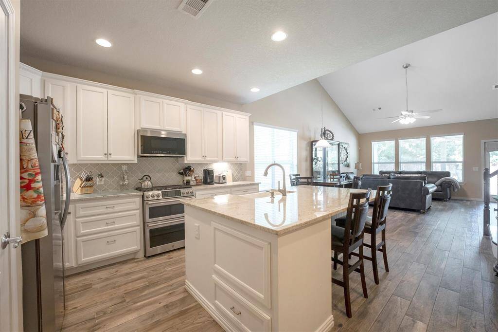 This fully loaded kitchen is a showstopper, featuring crisp white cabinetry with modern hardware, granite countertops, stylish backsplash, and stainless steel appliances—including a double oven. The expansive island offers extra prep space and seating, perfect for casual meals or gathering with guests. Open to the dining and living areas, this layout was designed for effortless entertaining and everyday comfort.