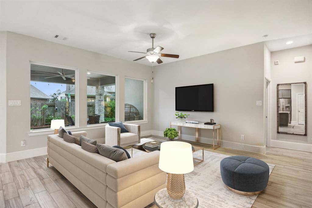 This inviting living room features modern furnishings and ample natural light from large windows overlooking a landscaped backyard. The open layout and neutral tones create a warm, welcoming atmosphere.
