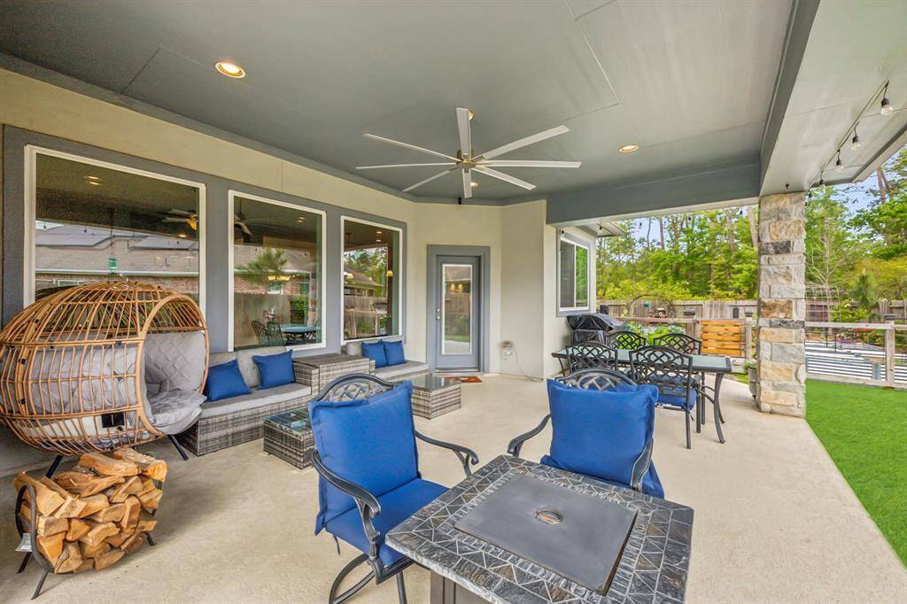 A spacious covered patio with comfortable seating, a modern ceiling fan, and a hanging chair, perfect for outdoor relaxation. The area features elegant stone accents and overlooks a green backyard, ideal for entertaining.