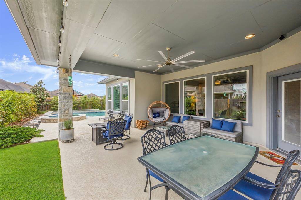 A spacious covered patio with comfortable seating, a ceiling fan, and a dining area, overlooking a landscaped yard with a pool and spa. Perfect for outdoor entertaining and relaxation.