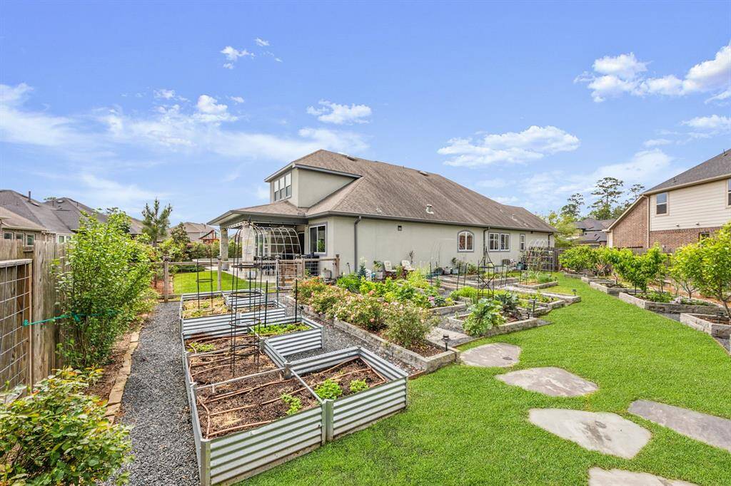 Charming backyard with a spacious garden featuring raised beds and lush greenery. The house has a cozy covered patio and ample lawn space, ideal for outdoor relaxation and gardening.