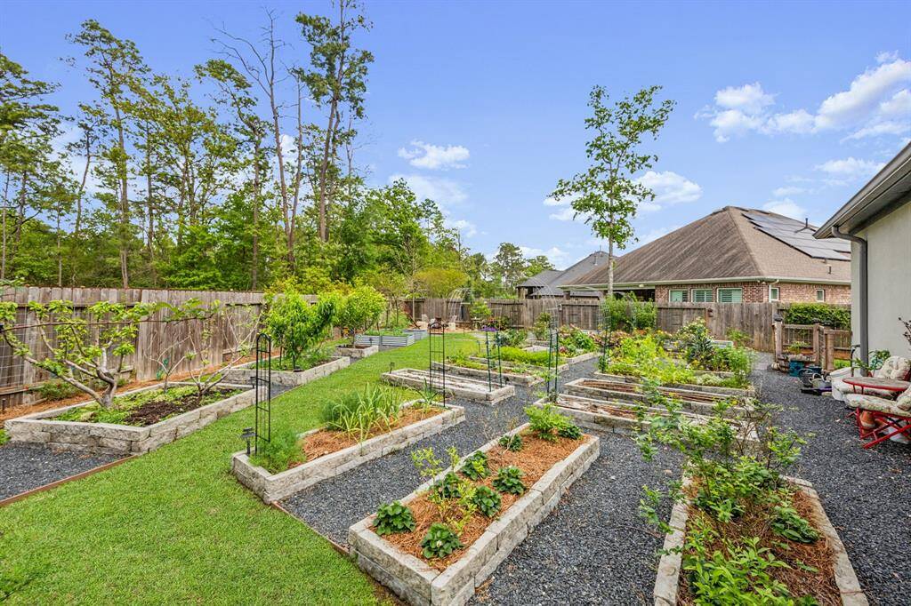 This backyard features a beautifully maintained garden with multiple raised beds, a well-kept lawn, and a backdrop of tall trees, offering a serene and private outdoor space perfect for gardening enthusiasts.