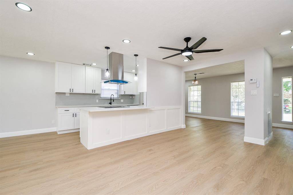 Enjoy your day in this bright, open-concept kitchen and living area features light wood flooring, a large half island with pendant lighting, a ceiling fan, and ample natural light from large windows. Space is also perfect for entertaining.