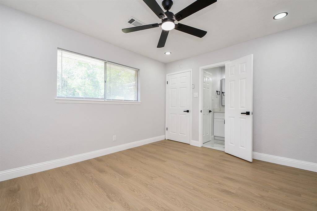 View of the primary bedroom downstairs featuring laminate wood flooring, a ceiling fan, and a large window for natural light.