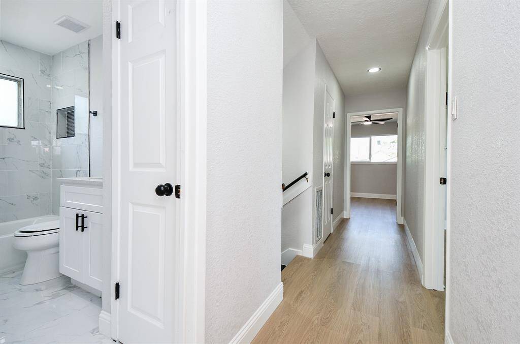 The bright hallway with light wood flooring connects to the bedrooms. On the left, is a modern bathroom featuring marble-style tiles and a white vanity.