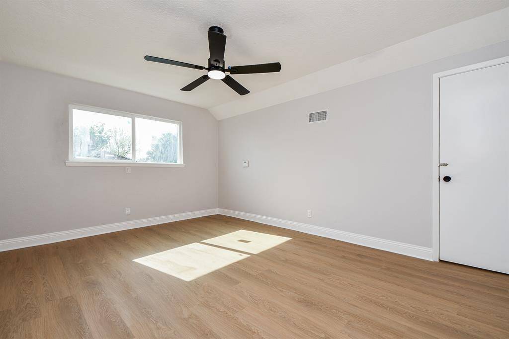 Bedroom 2. This bright, spacious room features light wood flooring, neutral walls, a ceiling fan, and a large window providing abundant natural light, perfect for a bedroom or office.