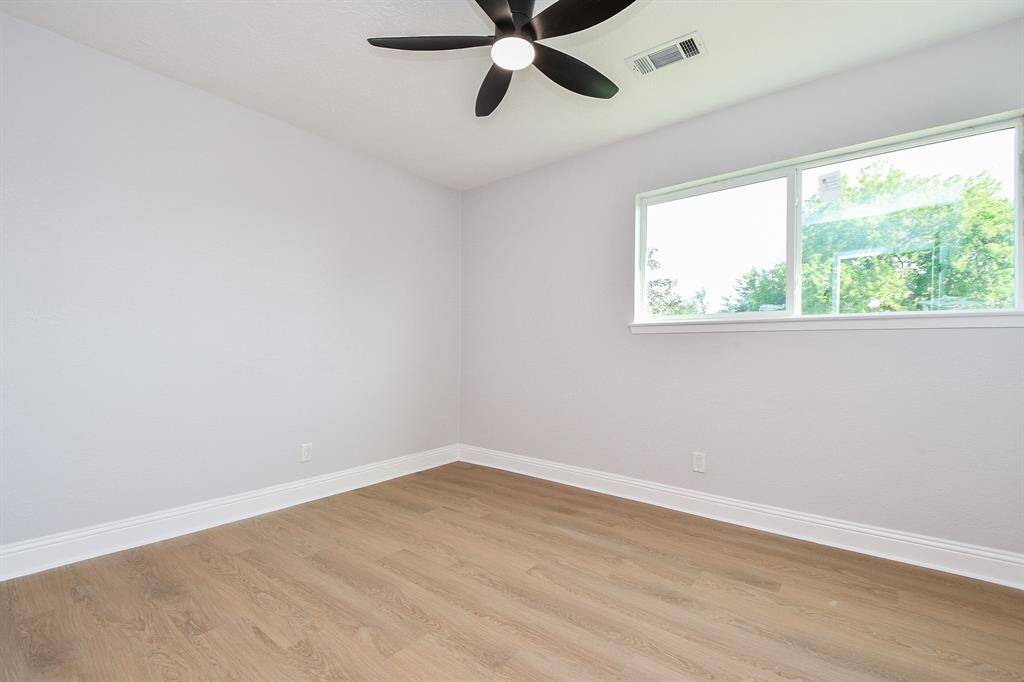 Bedroom 3. This room features light wood flooring, a large window providing ample natural light, and a modern ceiling fan. The neutral walls offer a blank canvas for personalization.