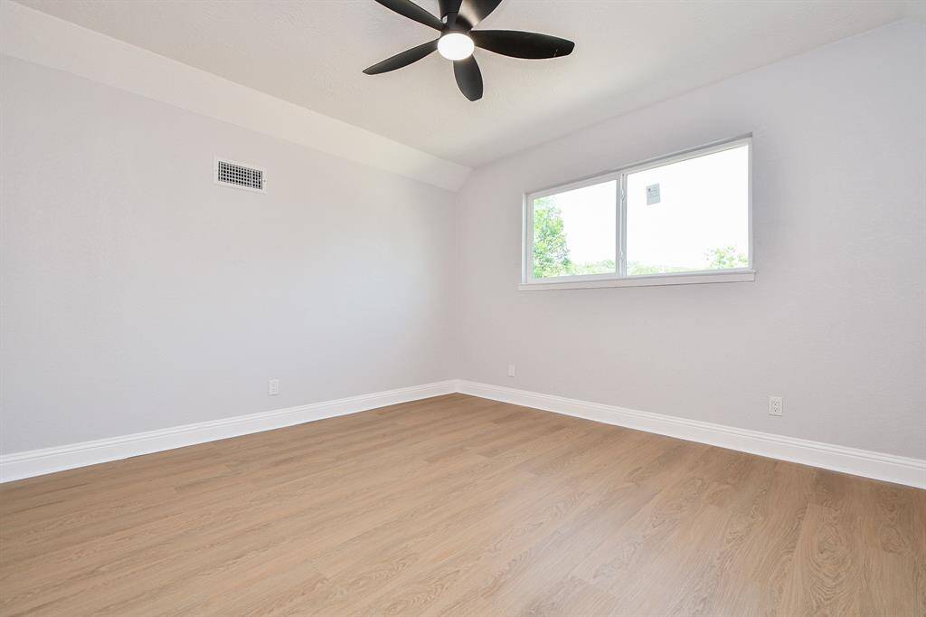 Bedrooom 4. This room features fresh light gray walls, wood-look flooring, a large window for natural light, and a modern ceiling fan. It's a bright and airy space, ideal for a bedroom or home office.