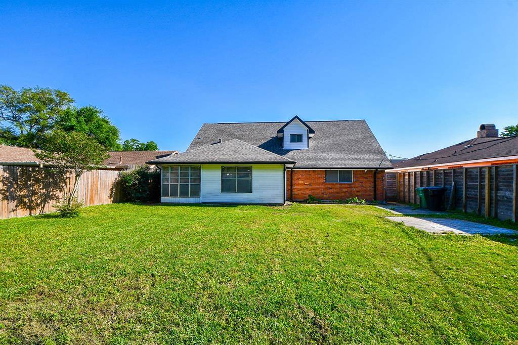 Spacious backyard with a well-maintained lawn, bordered by wooden fencing for privacy. The home features a brick exterior with a large extension offering ample natural light and potential for outdoor enjoyment.