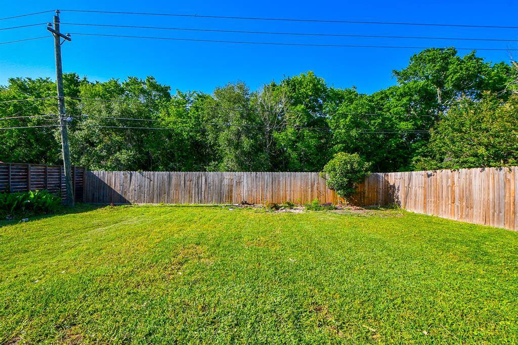 This spacious backyard with a green lawn, surrounded by a wooden fence and lush trees, provides privacy and a serene atmosphere here just waiting on YOU!