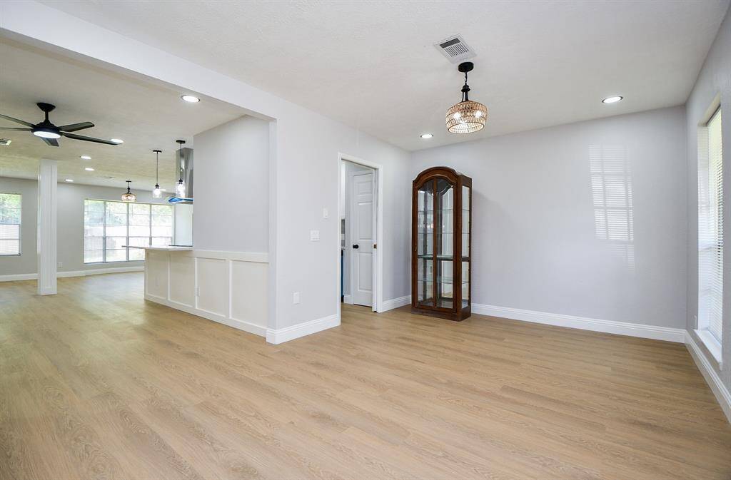 This home's bright, open-concept living space features light wood flooring, recessed lighting, and modern ceiling fans. The room connects seamlessly to a spacious dining area with large windows, offering plenty of natural light.
