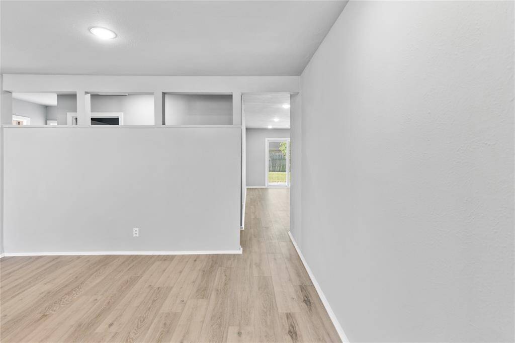 Bright, open hallway with light wood flooring and neutral walls in living room leading to dining room/ den.