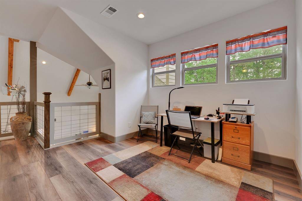 Charming loft office space with abundant natural light! This cozy workspace features three large windows, stylish wood flooring, and a modern railing overlooking the main living area.