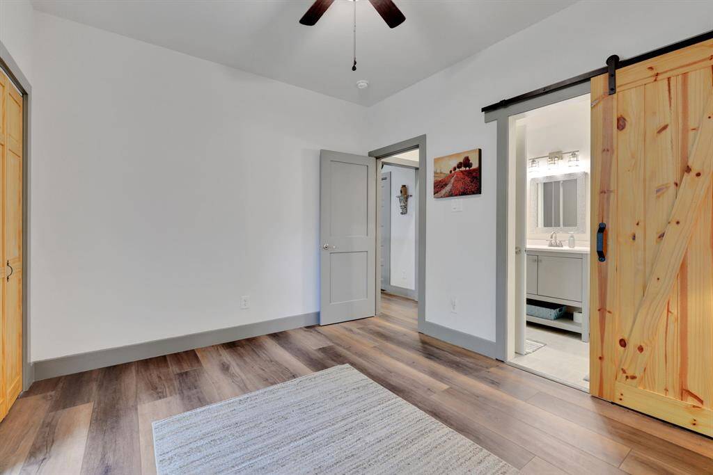 Inviting guest bedroom with en-suite bath. This cozy space features warm wood flooring, a rustic barn door leading to a beautifully designed bathroom, and soft neutral tones.