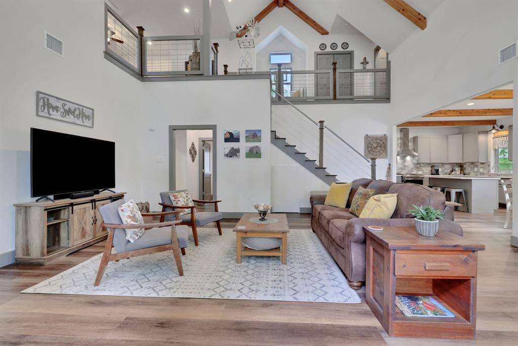 This open-concept living space is the perfect blend of modern farmhouse charm and cozy elegance, featuring vaulted ceilings, rustic beams, loft-style top floor, and a seamless flow into the kitchen.