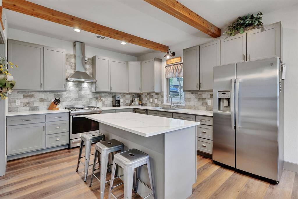 Stainless steel appliances, quartz countertops, backsplash, and the wood beams and luxury vinyl plank flooring all combine to create a sleek and modern aesthetic.