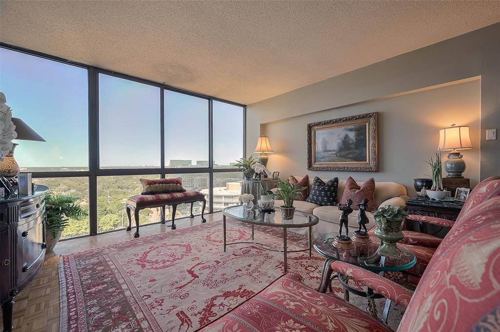 This living room features large floor-to-ceiling windows offering expansive views and abundant natural light. It's elegantly decorated with classic furniture, a plush red-patterned rug, and tasteful artwork, creating a cozy yet sophisticated atmosphere.