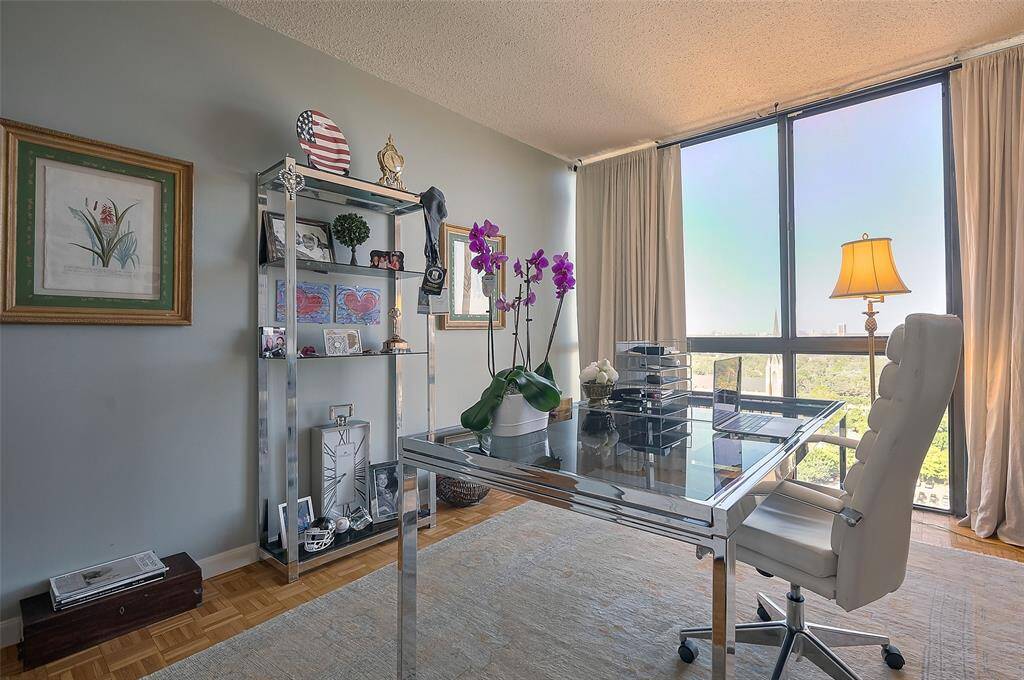 This bright, elegant home office features a glass desk, modern decor, and large windows with scenic views, providing a serene and productive workspace.