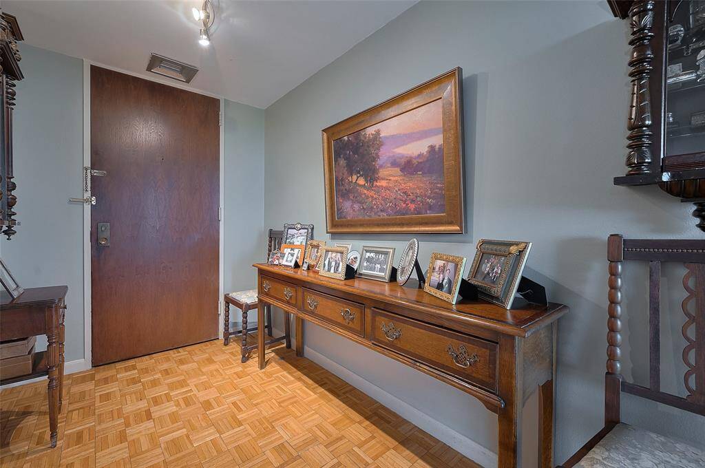 cozy entryway with a wooden door and parquet flooring. A classic console table holds framed photos and a landscape painting, creating a welcoming and personal atmosphere.