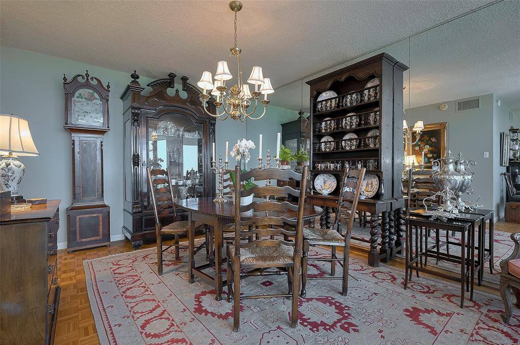 This elegant dining room features classic wooden furniture, including a large grandfather clock and a mirrored china cabinet. The space is adorned with a traditional rug and lit by a chandelier, exuding a vintage charm.