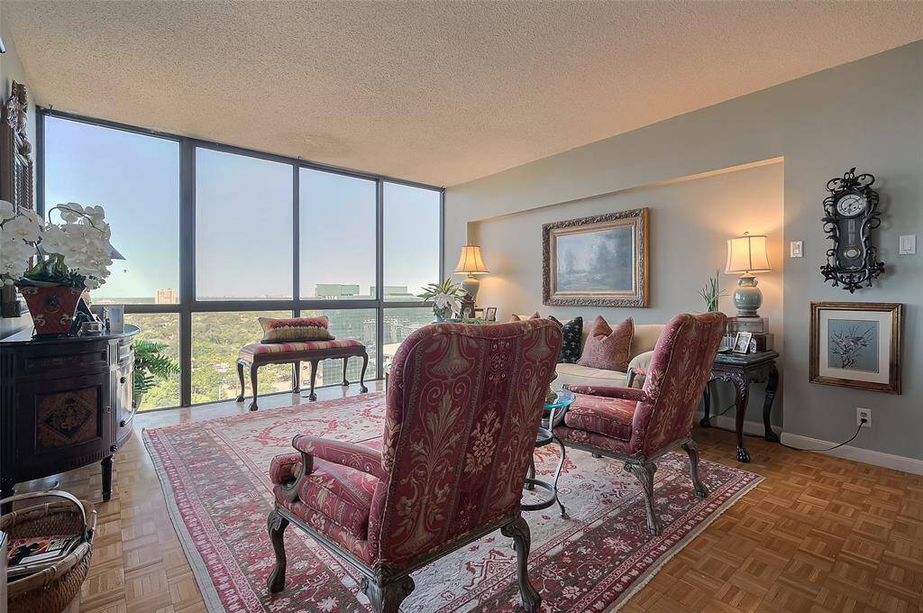 Bright living room with large windows offering a scenic view. Classic decor features patterned armchairs, a plush rug, and elegant wall art—cozy seating area with ambient lighting and parquet flooring.