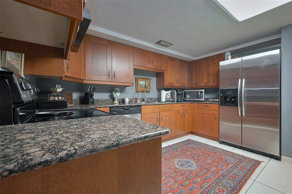 Spacious kitchen featuring sleek granite countertops, stainless steel appliances, and warm wood cabinetry. The room is complemented by a patterned rug and ample storage space, creating a stylish and functional cooking area.