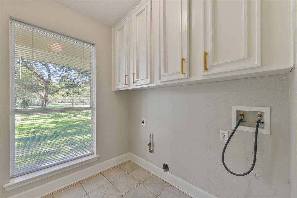 The utility room is convenient to the kitchen and it features upper cabinetry, tile floors, gas and electric hookups, and a sunlit window with blinds.