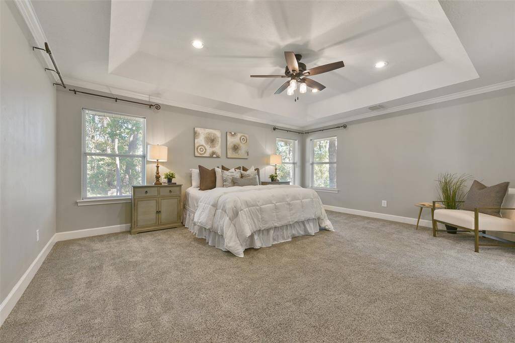 Escape to the secluded master suite and you'll find a trayed ceiling with a stylishly updated lighted ceiling fan, recessed lights, neutral paint, crown molding, plush carpet, and numerous windows with park-like views of the wooded property.