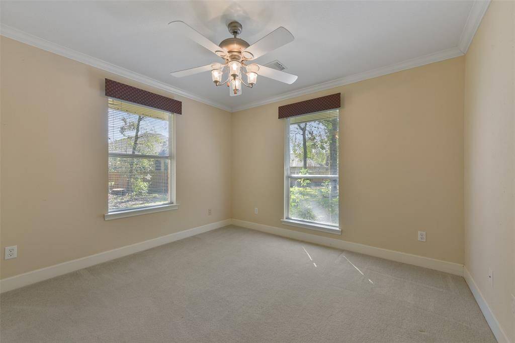The first of two identically sized secondary bedrooms that are located in this wing of the house showcases a lighted ceiling fan, neutral paint trimmed with crisp white crown molding, front and side facing windows, plush carpet, and a double door closet.
