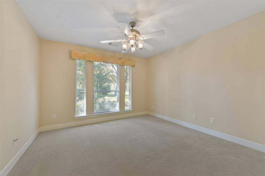 The second of two identically sized secondary bedrooms that are located in this wing of the house showcases a lighted ceiling fan, neutral paint trimmed with crisp white crown molding, a trio of front-facing windows, plush carpet, and a double-door closet.