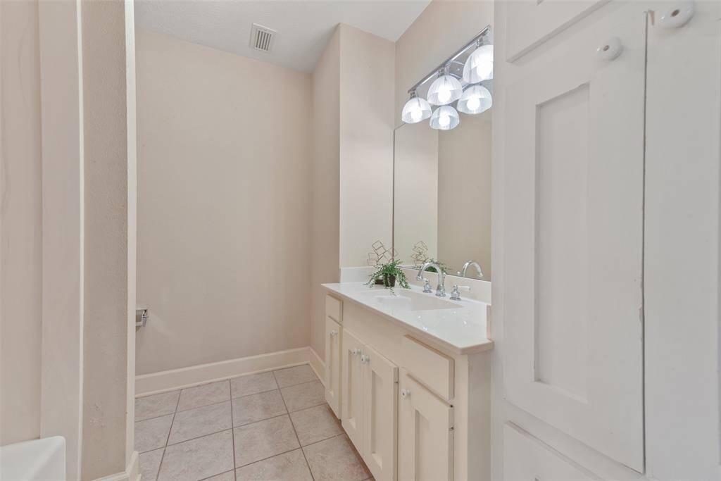 This bathroom services the previous two bedrooms and it boasts a cultured marble vanity with a rectangular basin sink, creamy white cabinetry, tile floors, neutral paint, and a combination bathtub and shower with a cultured marble surround.