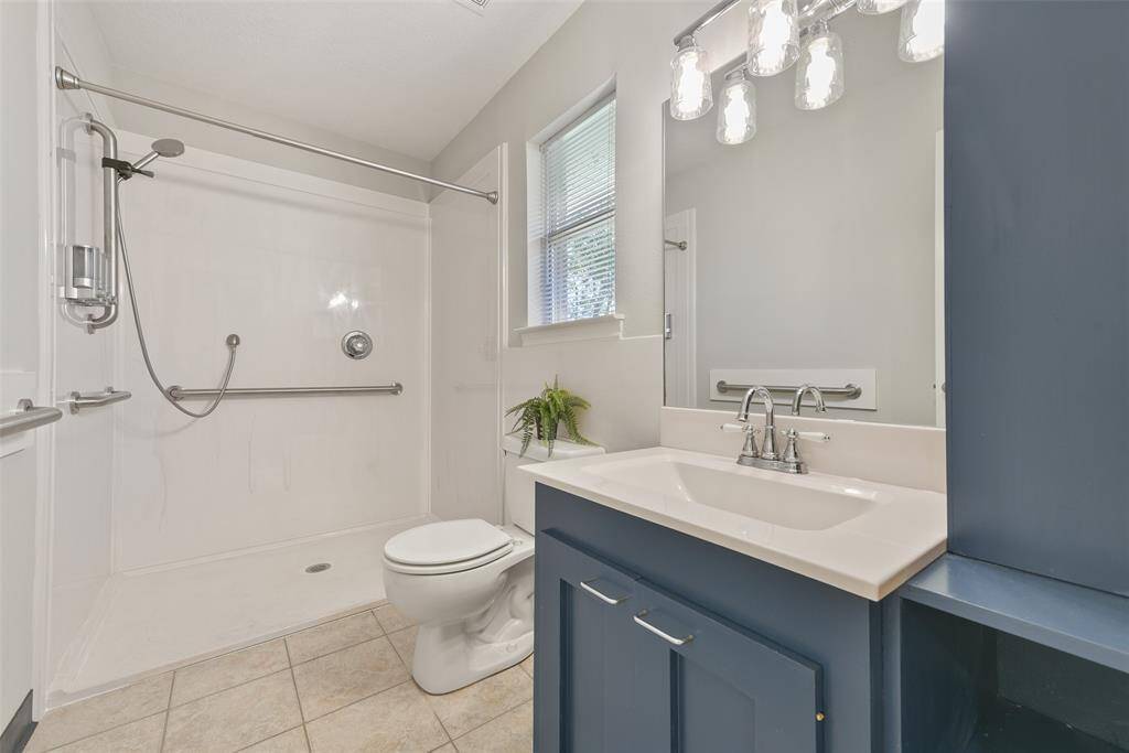 This handicap-accessible bathroom is adjacent to the bonus room and here, you'll find a zero-entry shower with a handheld showerhead and grab bars, a lowered rectangular basin sink with a cultured marble countertop, and beautiful dusty blue cabinetry.