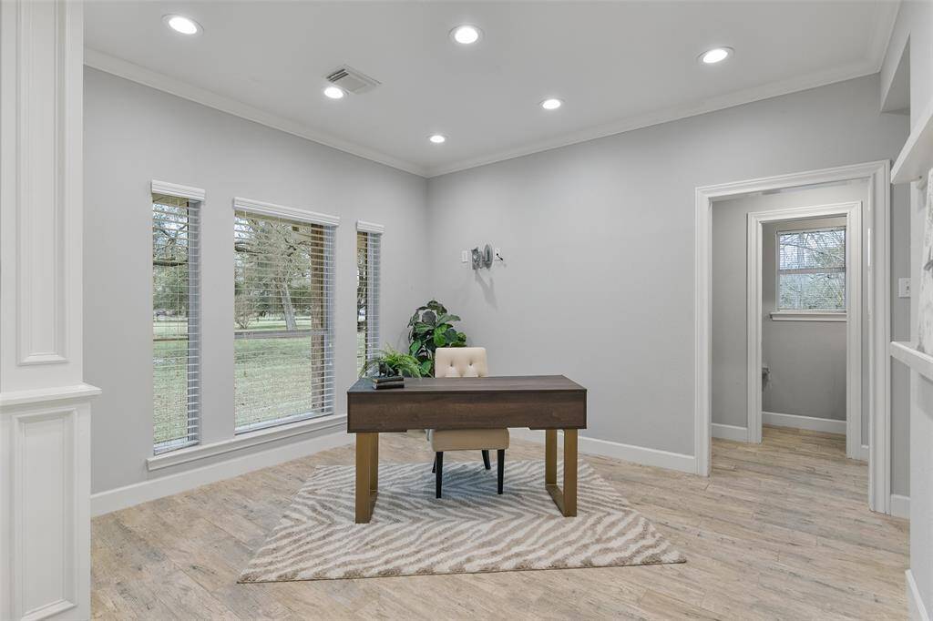 To the left of the foyer, a wide entrance opens into this flexible space that could serve as an office, a dining room, or a sitting room. It boasts recessed lights, grey paint, crisp white crown molding, and a trio of double-paned windows overlooking the front yard.