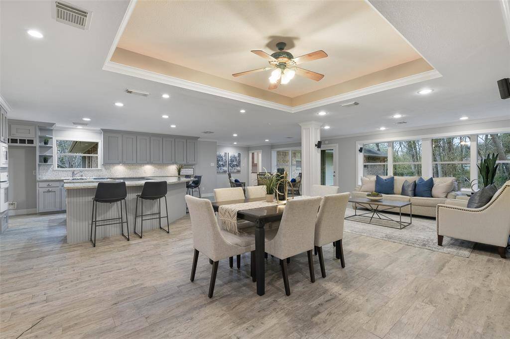 Continue straight ahead from the foyer into this magnificent open-concept living space. It has a trayed ceiling with a lighted ceiling fan, recessed lights, easy-care wood-look tile floors, and a wall of windows with views of the sprawling wooded property.