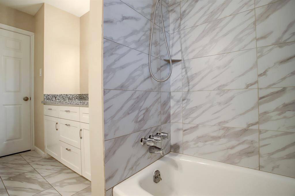 View of tub and attractive tiled areas in guest bathroom. Brushed nickel hardware.