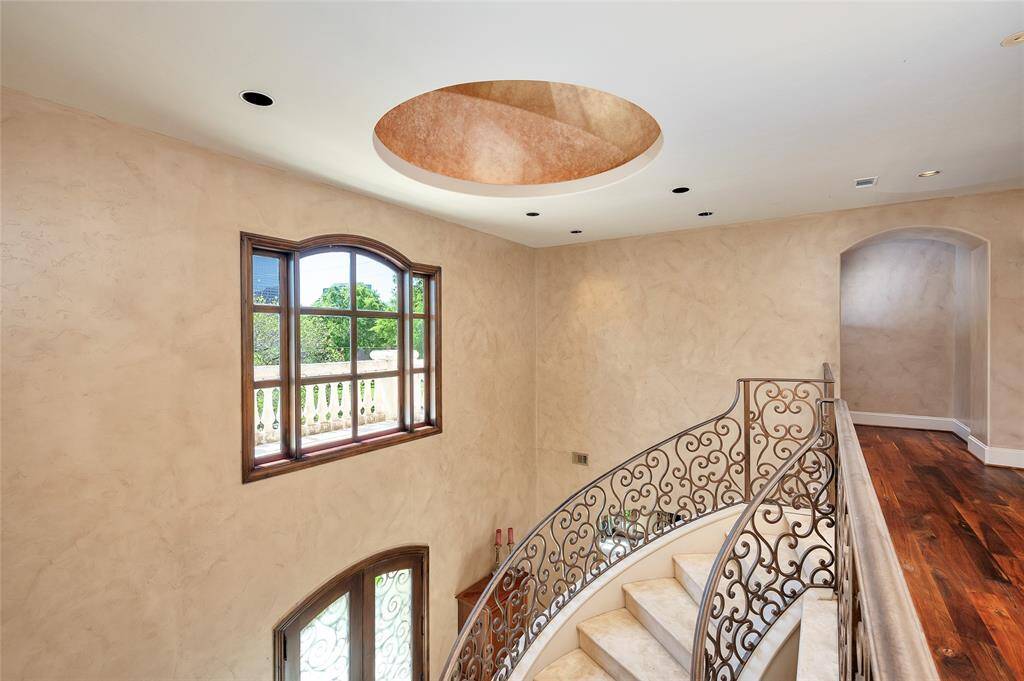 A view of the upper landing overlooking the foyer with a lighted dome ceiling, arched window with views of greenery, and arched glass-paneled wooden French entry doors with wrought iron overlays. Additional features include recessed lighting, faux finished walls, and hardwood flooring on the landing.