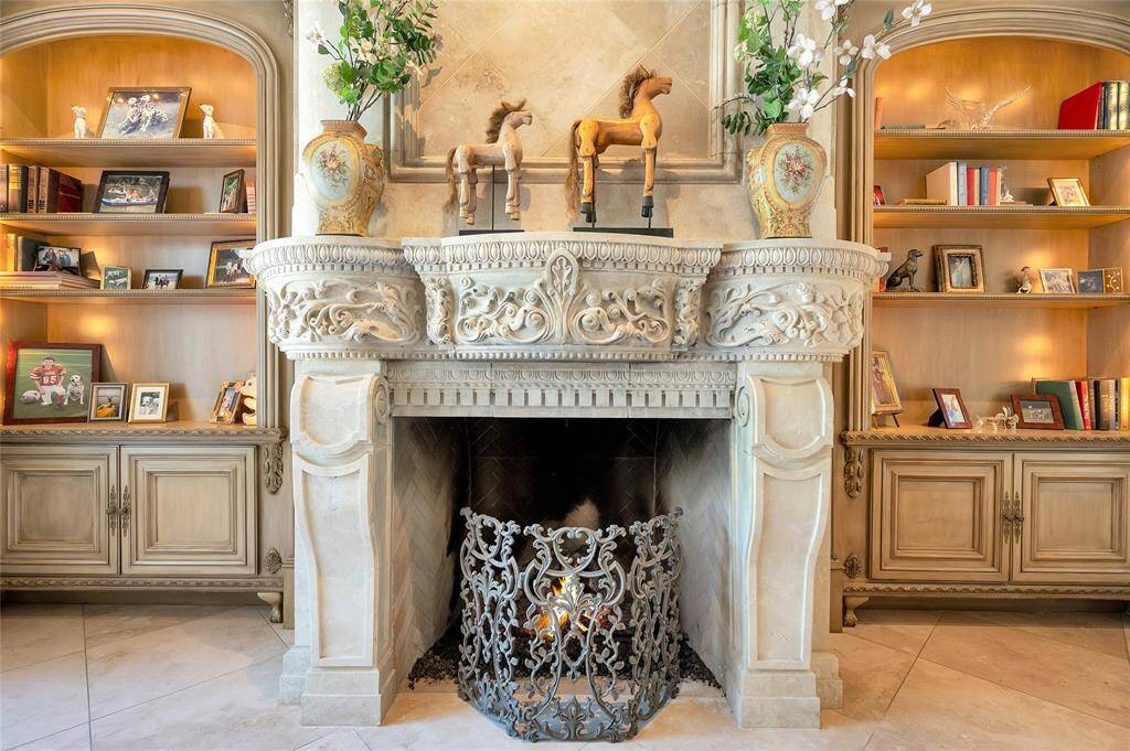 A closer look at the captivating formal living room limestone fireplace with intricate stonework, flanked by lighted arched wooden built-ins with adjustable shelving.