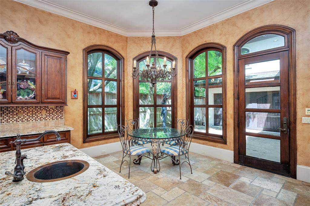 Open to the kitchen, the breakfast room offers travertine tile flooring, 11” baseboards, double crown molding, and wrought iron chandelier lighting. A wall of arched windows provides abundant natural light, while the glass-paneled wooden exterior door with an arched transom provides access to the back driveway.
