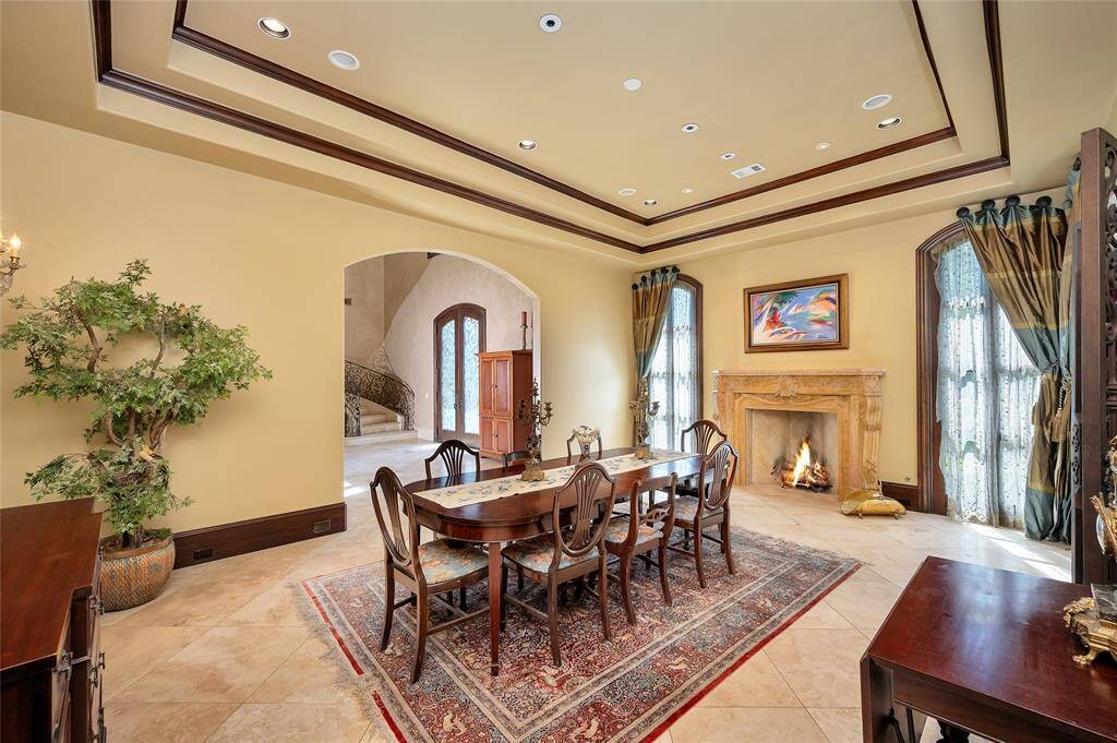The formal dining room boasts a double tray ceiling with wood-stained crown molding, recessed and art lighting, surround sound, dual crystal wall sconces, arched floor-to-ceiling windows, 11” baseboards, and travertine tile flooring. A gorgeous hand-carved solid marble fireplace provides a warm and inviting feel to the space.