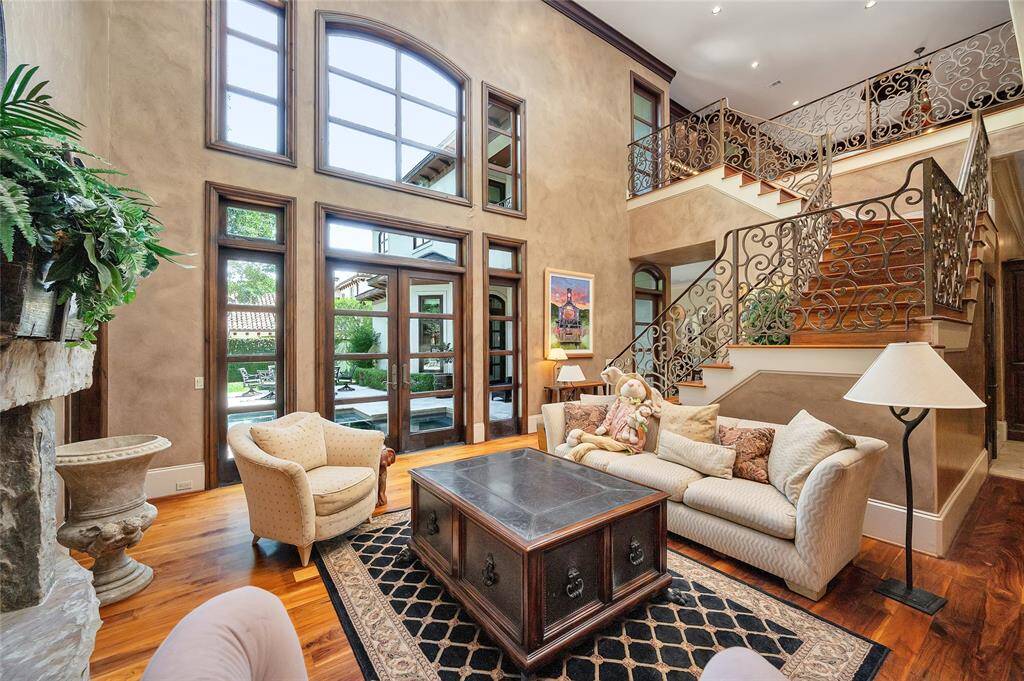The spacious family room features a 24-foot ceiling, double crown molding, recessed lighting, surround sound, multiple double-height windows with pool views, 11” baseboards, and hardwood flooring. A grand staircase with ornate iron railings leads to the upstairs gameroom, while glass-paneled wooden French doors open to the backyard, creating a seamless indoor-outdoor living experience.
